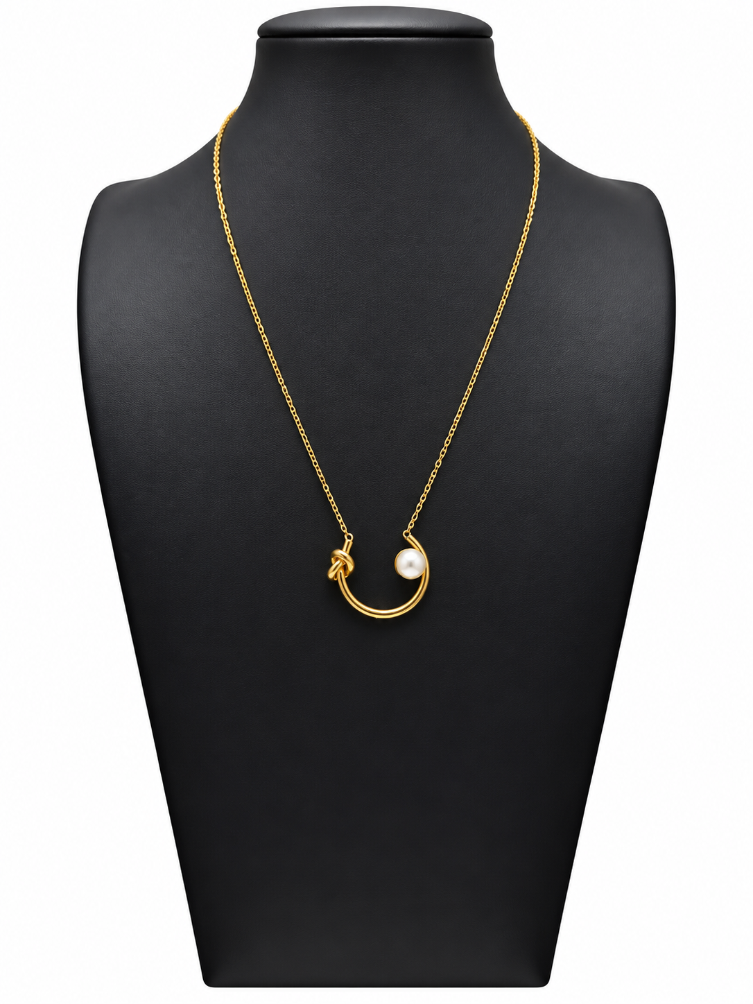 Collar dorado de mujer con colgante curvo abierto, nudo decorativo y perla blanca, sobre expositor negro y fondo blanco