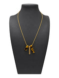 Collar de mujer de cadena dorada fina con tres piezas colgantes, dos de efecto carey y una barra dorada, sobre busto negro y fondo blanco