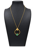Collar dorado de mujer con aro circular, detalle floral superior y pieza verde redonda en la parte inferior sobre expositor negro y fondo blanco